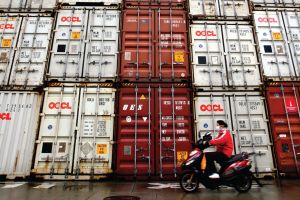 A woman rides her motorcycle past containers at the Port of Shanghai.