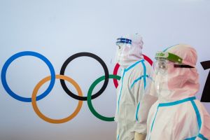 Two figures in full body medical protective suits walk in front of the Olympic rings in the Beijing airport.