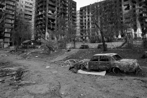 Black and white photo of a destroyed car and apartment buildings in Ukraine