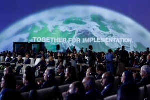 Crowd of people at COP27 in front of a screen with earth's curve and writing saying "together for implementation."