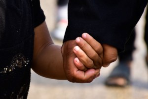 Adult and child hands holding, both in dark shirts. 