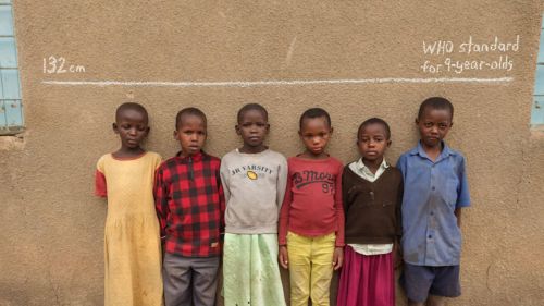 Children in Tanzania stand below a line showing the median height for 9-year-olds globally