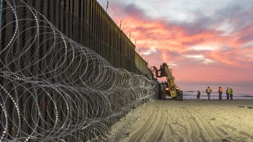U.S. Border Patrol Agents at Border Field State Park in San Diego watch over personnel reinforcing the border fence with concertina wire