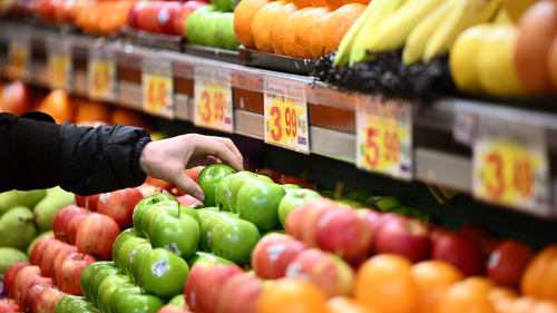 A person reaches to grab a green grape from a shelf of fruit in a grocery store.