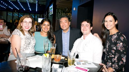 Five people smiling stand around a table with food and drinks