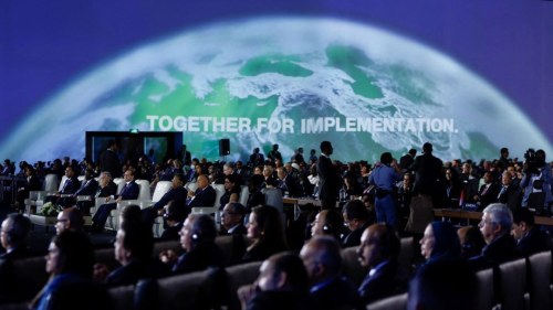 Crowd of people at COP27 in front of a screen with earth's curve and writing saying "together for implementation."