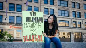 A young woman in Delaware holds a sign saying, "No human being is illegal"