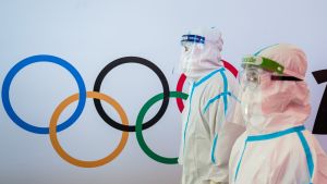 Two figures in full body medical protective suits walk in front of the Olympic rings in the Beijing airport.