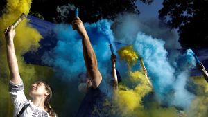 People hold flares with the colors of the Ukrainian flag at a protest against the Russian invasion.