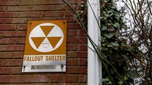 Fallout shelter sign on brick wall next to trees.