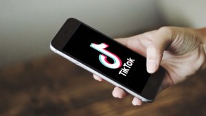 Hand holding cell phone with TikTok logo on the screen. 