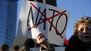a woman holds a sign with NATO crossed out